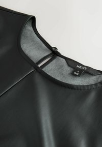 Sort faux læder top med en glat tekstur, rund halsudskæring og udskæring bagpå, sikret med en knap. Mærke synligt indeni.