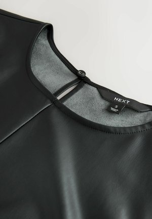 Czarna bluzka z sztucznej skóry o gładkiej fakturze, okrągłym dekolcie i wycięciem z tyłu, zabezpieczonym guzikiem. Etykieta widoczna wewnątrz.