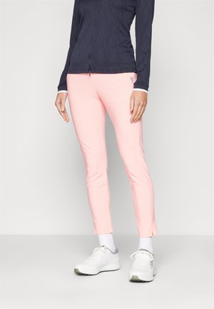 Pantalons ajustés rose clair avec un motif texturé, associés avec un haut à manches longues bleu foncé. Les chaussures sont blanches avec des accents gris.