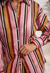 Gestreepte blouse in roze, oranje en zwart; gemaakt van lichte stof met een zachte textuur, voorzien van een knoopsluiting aan de voorkant en een puntige kraag.