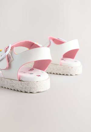 Hvide sandaler med en pink rem, mønstrede indlægssåler og teksturerede såler. Har en tyk, tekstureret bund med et minimalistisk design.