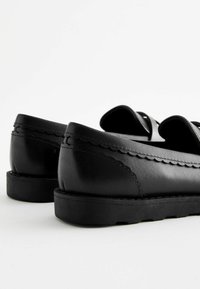Černé kožené boty s hladkým povrchem, vlnitým detailem podél okraje a silnou černou gumovou podrážkou. Nízkoprofilový design.