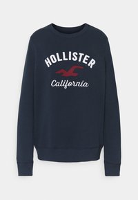 Marinblå sweatshirt med rund hals, långa ärmar, med vit "HOLLISTER" text och röd "California" broderad under.