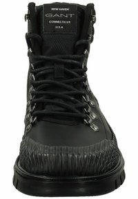 Black hiking boot featuring a textured rubber upper, smooth leather accents, metal eyelets, and a wide, ridged sole for traction.