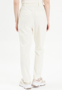 Pantalons blancs, fuselés, avec une texture lisse et deux poches arrière. Portés avec des baskets de couleur claire au design volumineux.