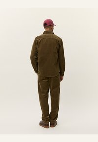 Braunes Cordhemd und Hosen-Set mit relaxed Fit. Die Rückansicht zeigt einen Kragen und Knopfdetails. Abgerundet mit braunen Schuhen.