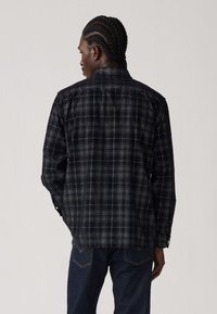 Black and gray plaid flannel shirt with long sleeves and a collar. Features buttons at the cuffs and back yoke design.