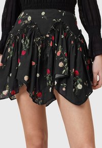 Saia preta floral com bainha assimétrica, decorada com padrões de rosas vermelhas e brancas. Feita de tecido leve com uma textura suave.