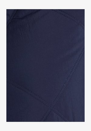 Marineblauwe gewatteerde stof met een ruitenpatroon en zichtbare stiksels. De textuur lijkt glad met een lichte glans.