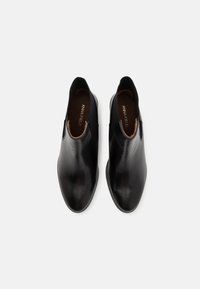 Bottines noires en cuir sans lacets avec bouts en forme d'amande et panneaux latéraux élastiques, vues de dessus sur fond blanc.