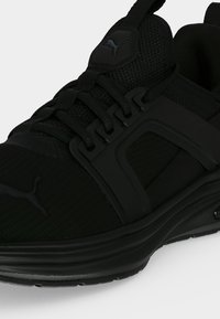 Μαύρο αθλητικό παπούτσι Puma με δίχτυ πάνω μέρος, δέσιμο με κορδόνια μπροστά και λογότυπο στη γλώσσα και στο πλάι, εμφανίζεται από κοντινή πλευρική γωνία.