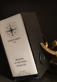 Gezichtserumgeldoos met een wit label, zwart kardoezen lichaam, kompaslogo en tekst die productdetails aangeeft in een minimalistisch ontwerp.