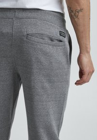 Gray sweatpants made of soft cotton blend, featuring a back pocket, elastic waistband, and smooth texture. Label visible near pocket.