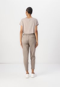 Beige kortermet topp med avslappet passform, kombinert med lysegrå tapered bukser som har elastisk midjebånd og to baklommer.