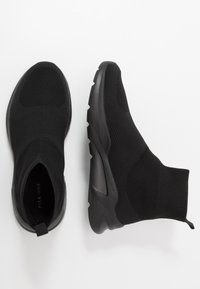 Černé pletené slip-on boty s horní částí podobnou ponožce, texturovaným materiálem a silnou gumovou podrážkou. Obsahuje poutko na patě pro snadné obouvání.