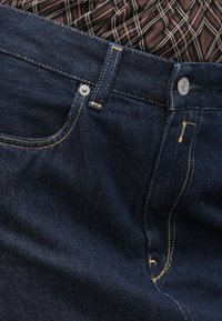 Jeans in denim blu scuro con taglio dritto, cuciture dorate, chiusura con bottone in metallo e tasca frontale con dettagli di cucitura visibili.