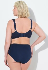 Námořnická modrá podprsenka s nastavitelnými ramínky a třístupňovým zapínáním na zádech, spárovaná s vysokými námořnickými kalhotkami s jednoduchým designem a švy.