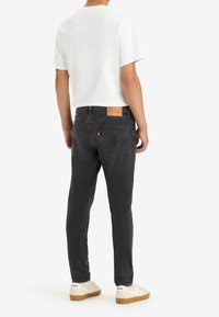 Svarta denimjeans med rak passform, med en läderetikett vid bakre midja och en subtil blekt textur, ihop med en vit T-shirt.