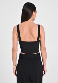 Top nero corto con spalline larghe, texture liscia e design con schiena bassa abbinato a pantaloni neri a vita alta.