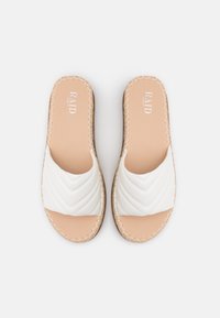 Sandales blanches à glissière avec un design supérieur matelassé, semelle intérieure beige, détails de couture sur les bords et semelle plate. Légères et décontractées.