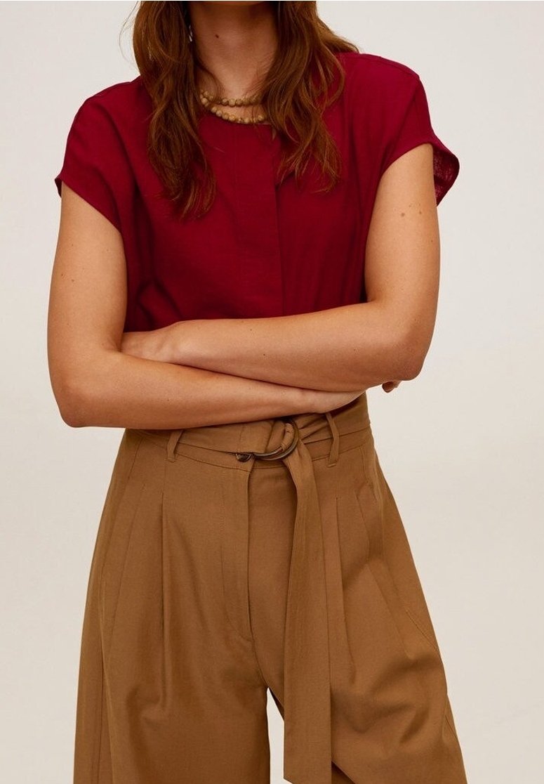 Top rojo de manga corta con cuello redondo, combinado con pantalones de pierna ancha en tono beige de cintura alta sujetados con un cinturón. Textura de tela suave.