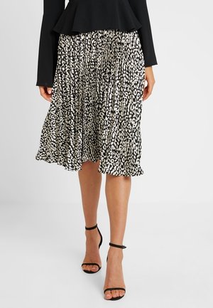 Zwart-witte midi-rok met plooien, een vloeiende silhouet en zachte stof. Gecombineerd met zwarte sandalen met bandjes.