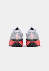 Chaussures de course avec une tige en maille grise, semelle extérieure noire et corail, accents arrière blancs, talon texturé pour une meilleure adhérence et col de cheville rembourré.