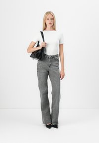 Sac en cuir noir en forme triangulaire, haut blanc à manches courtes, et jean gris taille haute avec une coupe décontractée et une texture subtile.