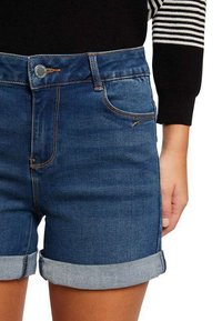 Shorts in denim con un lavaggio blu scuro, con risvolto, dotati di cinque tasche, cuciture a contrasto e chiusura con bottone in metallo.