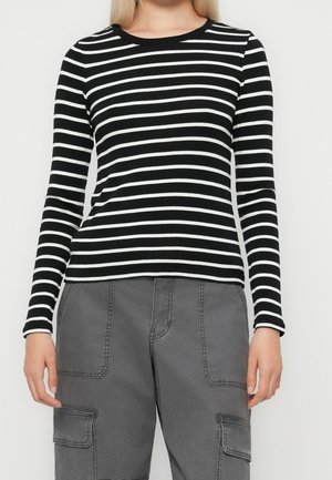 Kvinde iført en sort-hvid, vandret striped langærmet trøje og grå cargobukser med store forlommer.