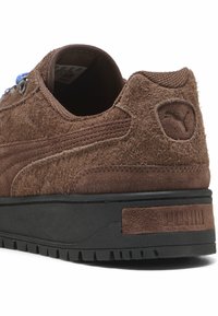 Izgatavoti no brūna zamša, šie sporta apavi ir ar teksturētu virsmu, melnu gumijas zoli un ziliem sasienamajiem aukliņām. Satur logotipa uzlīmi un pastiprinātas acu caurumiņus.