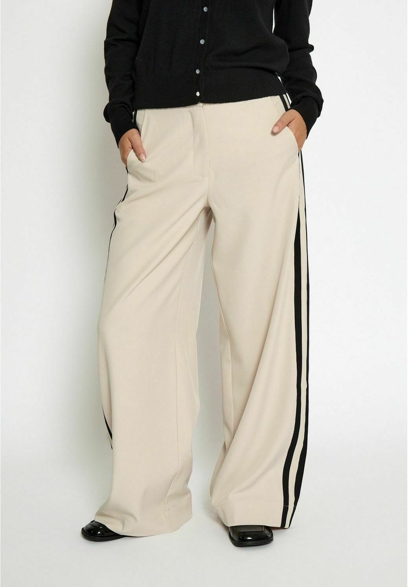 Beige wide-leg trousers with black side stripes, featuring side pockets and a smooth, lightweight fabric. Paired with a black button-up cardigan.