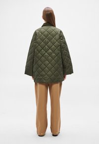 Pihe-puha olívazöld dzseki laza szabással, gallérral és széles ujjakkal. Bézs nadrág fölött viselve.