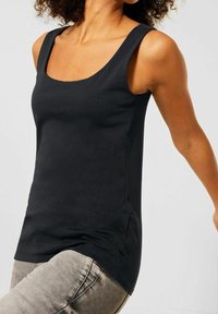 Svart ärmlös linne med rundad halsringning, tillverkat av slät tyg. Har en åtsittande design och subtila sidonämsdetaljer.