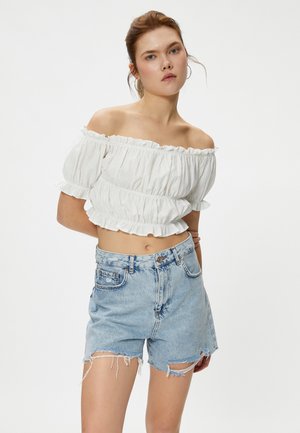 Witte off-the-shoulder top met gerimpelde randen, gecombineerd met lichtblauwe high-waisted denimshorts met een franjes zoom en verwerkte details.