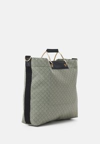 Torba na ramię z teksturowanego zielonego materiału z geometrycznym wzorem, z czarnymi akcentami i złotymi elementami, zaprojektowana z dwoma uchwytami na górze.