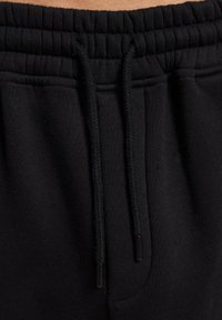 Svarte joggebukser med teksturert, elastisk midjebånd og justerbare snorer. Glatt stoff med sidelommer.