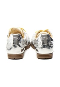 Zapatillas plateadas metálicas con cordones amarillos, que presentan una superficie texturizada y un logotipo en el talón, además de una suela de goma marrón.