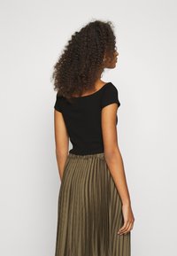 Mustat ribattut crop-topit, joissa on lyhyet hihat, yhdessä korkeavyötäröisen, laskostetun oliivinvihreän hameen kanssa. Teksturoitu kankaan yksityiskohta näkyvissä.