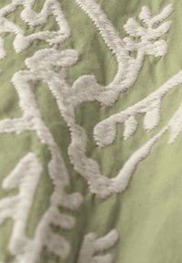 Tessuto verde chiaro con motivi floreali ricamati in bianco, caratterizzato da intricate spirali e forme di foglie per texture e dettaglio.