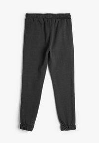 Pantalones de chándal negros de tela suave, con cintura elástica y puños elásticos en los tobillos, diseñados para la comodidad y facilidad de movimiento.