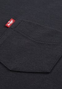 Fekete pamut póló zsebbel, tetején piros címkével. Az anyag puha tapintású, egyszerű és tiszta kialakítású.