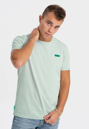 Camiseta de algodón de manga corta en color verde claro con cuello redondo, que presenta un pequeño parche rectangular verde en el pecho y un dobladillo recto.