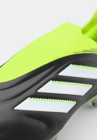 Black and neon green soccer cleat with a textured upper, three white serrated stripes, and a snug fit design. Accents include a shiny finish.