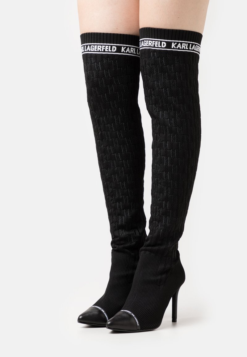 Bottes en tricot noires jusqu'à la cuisse avec des talons aiguilles, un motif texturé, des embouts en cuir, et des poignets élastiques brandés "KARL LAGERFELD".