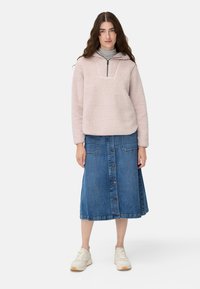 Pull polaire rose clair avec une demi-fermeture éclair, associé à une jupe en jean avec des boutons sur le devant et deux poches. Chaussures : baskets blanches.