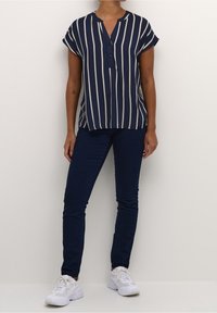 Chemise bleu marine à manches courtes avec des rayures verticales beige, col en forme de goutte et boutons ; associée à un jean skinny bleu foncé et des baskets blanches.
