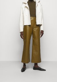 Biała kurtka z kapturem, brązowy sweter wzorzysty, szerokie oliwkowe skórzane spodnie oraz czarne szpilki. Prosty i strukturalny design.