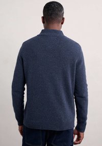 Marinblå klädd tröja med ribbad krage, texturerad tyg med flerfärgade fläckar, och en avslappnad passform med förlängda ärmar.