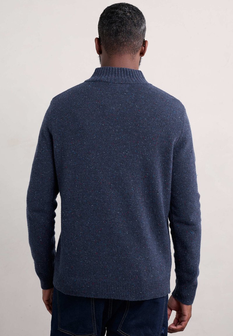 Marinblå klädd tröja med ribbad krage, texturerad tyg med flerfärgade fläckar, och en avslappnad passform med förlängda ärmar.